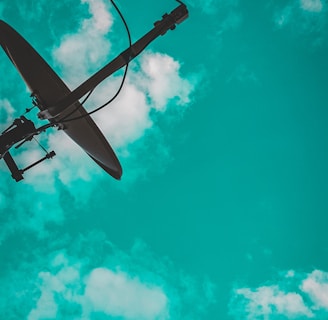 A satellite dish is silhouetted against a vibrant turquoise sky with scattered white clouds.